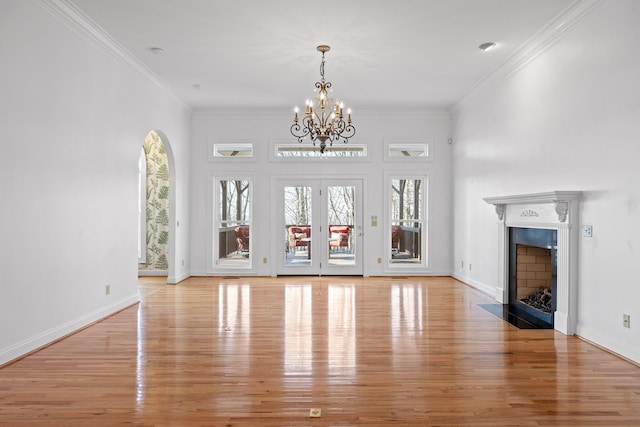 unfurnished living room featuring baseboards, a fireplace with flush hearth, crown molding, french doors, and light wood-style floors