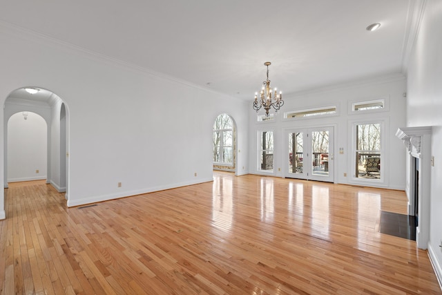 unfurnished living room with a fireplace with flush hearth, arched walkways, visible vents, and ornamental molding