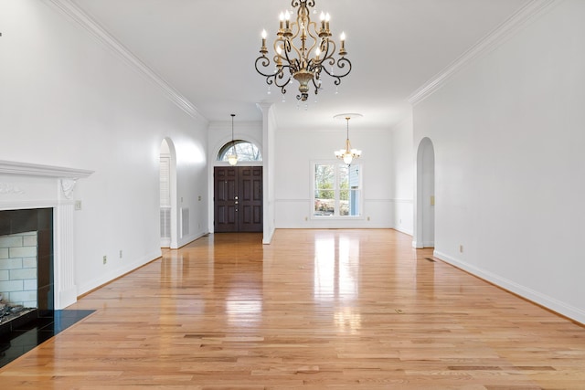 foyer entrance featuring arched walkways, light wood-style flooring, a notable chandelier, a fireplace with flush hearth, and baseboards