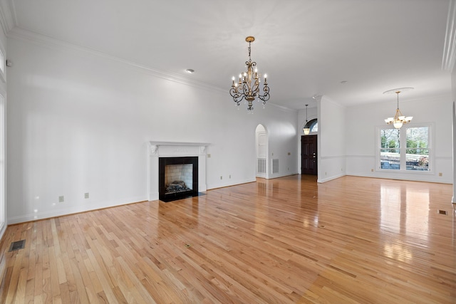 unfurnished living room with a fireplace with flush hearth, visible vents, ornamental molding, light wood finished floors, and an inviting chandelier