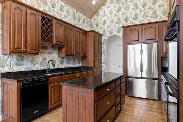 kitchen featuring wallpapered walls, dark stone countertops, vaulted ceiling, black appliances, and a sink