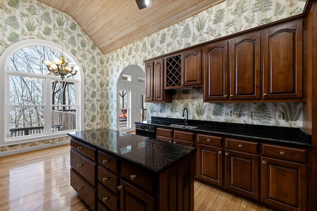 kitchen with wallpapered walls, dark stone countertops, dark brown cabinets, and a sink