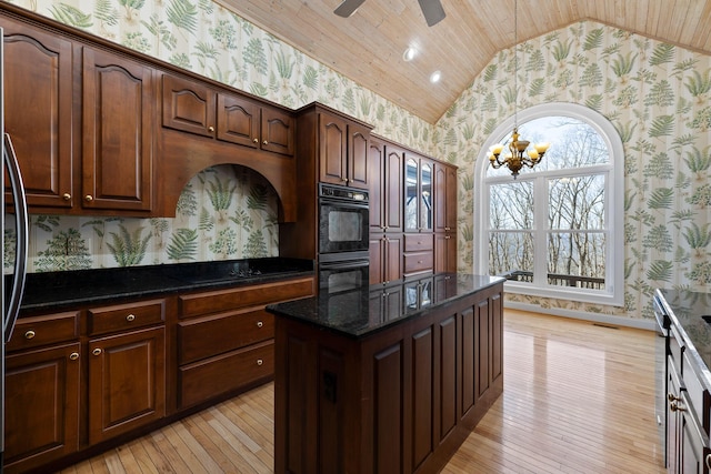 kitchen with lofted ceiling, light wood-type flooring, dark stone counters, black appliances, and wallpapered walls