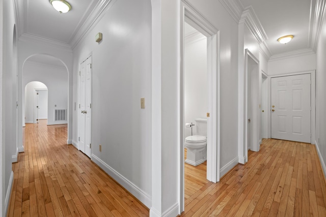 hallway with arched walkways, light wood-type flooring, baseboards, and crown molding