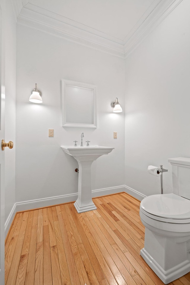 half bathroom featuring ornamental molding, toilet, baseboards, and wood finished floors