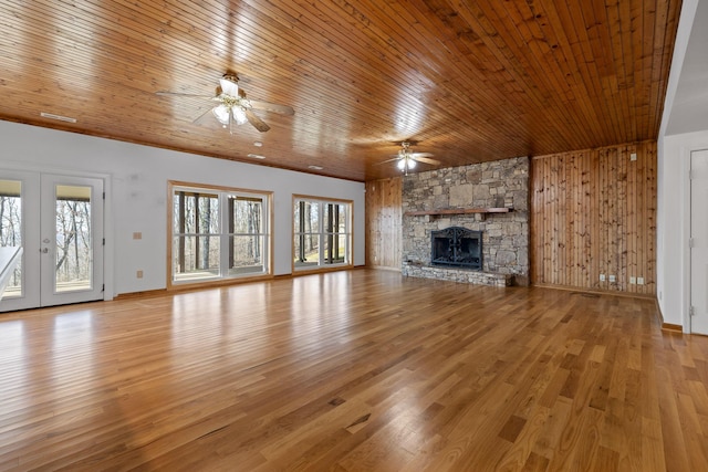 unfurnished living room featuring a stone fireplace, wooden ceiling, a ceiling fan, french doors, and light wood finished floors