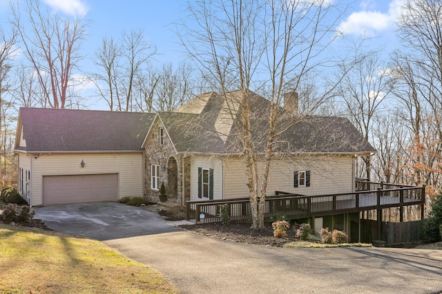 view of front of home with a garage, driveway, a chimney, and a wooden deck