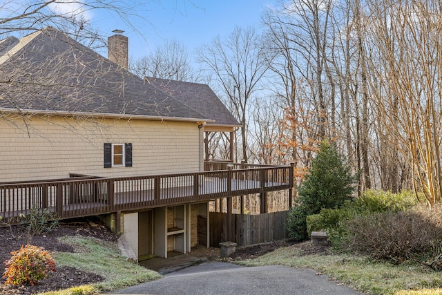 back of property with a shingled roof, a chimney, fence, and a wooden deck