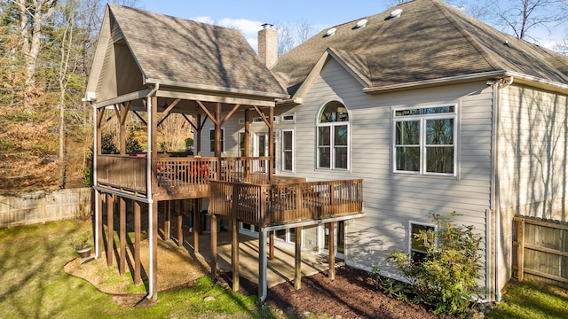 rear view of house with a chimney, a shingled roof, a lawn, fence, and a deck