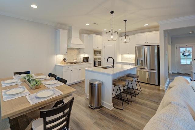 kitchen with white cabinetry, premium range hood, appliances with stainless steel finishes, and pendant lighting