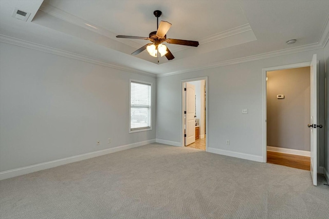 unfurnished bedroom with ceiling fan, connected bathroom, a tray ceiling, ornamental molding, and light carpet