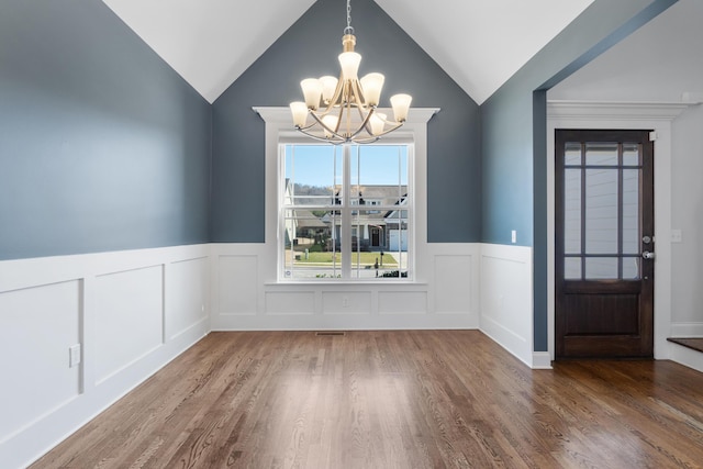 unfurnished dining area with hardwood / wood-style flooring, vaulted ceiling, and an inviting chandelier