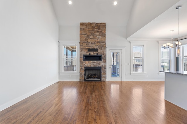 unfurnished living room with high vaulted ceiling, hardwood / wood-style floors, an inviting chandelier, and a stone fireplace