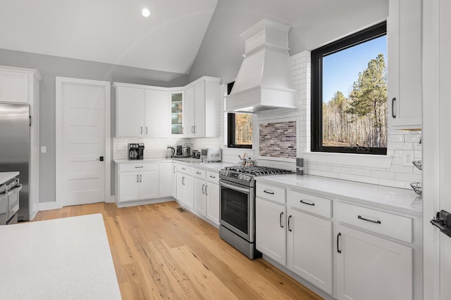 kitchen featuring lofted ceiling, stainless steel appliances, custom range hood, white cabinets, and light wood-type flooring