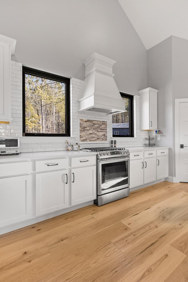 kitchen featuring light hardwood / wood-style flooring, stainless steel gas stove, white cabinetry, tasteful backsplash, and custom exhaust hood