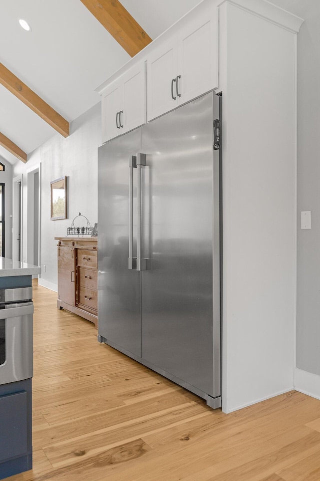 kitchen with appliances with stainless steel finishes, beam ceiling, light wood-type flooring, and white cabinets