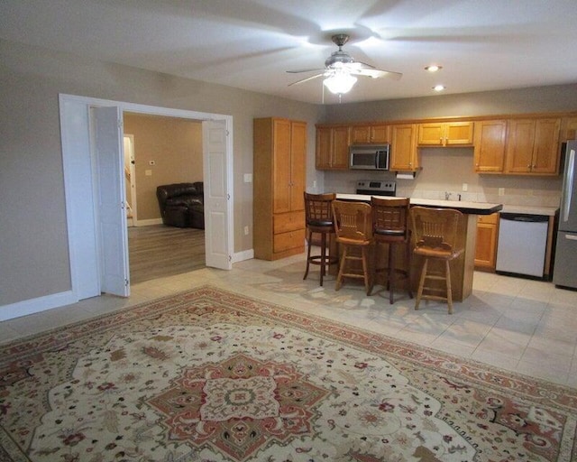 kitchen with a breakfast bar area, a center island, light tile patterned floors, appliances with stainless steel finishes, and ceiling fan