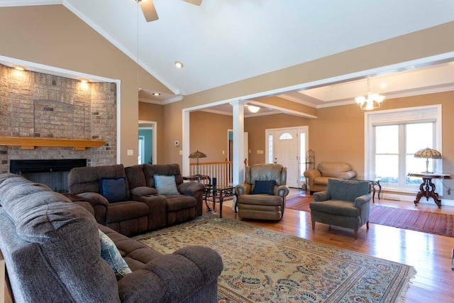 living room featuring crown molding, high vaulted ceiling, a fireplace, wood-type flooring, and ceiling fan with notable chandelier