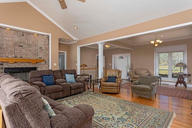 living room with crown molding, hardwood / wood-style flooring, high vaulted ceiling, a brick fireplace, and ornate columns