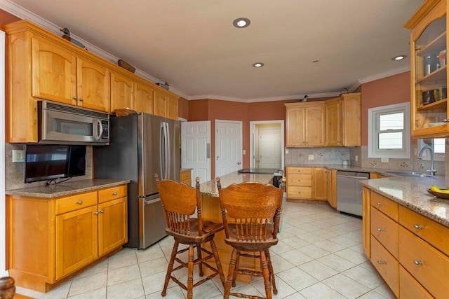 kitchen with sink, light stone counters, ornamental molding, appliances with stainless steel finishes, and backsplash