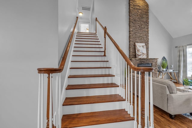 staircase featuring a brick fireplace, wood-type flooring, and high vaulted ceiling