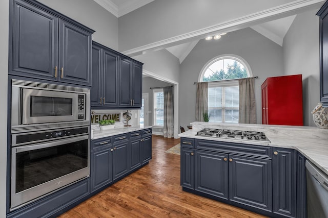 kitchen with lofted ceiling, dark wood-type flooring, appliances with stainless steel finishes, ornamental molding, and blue cabinets