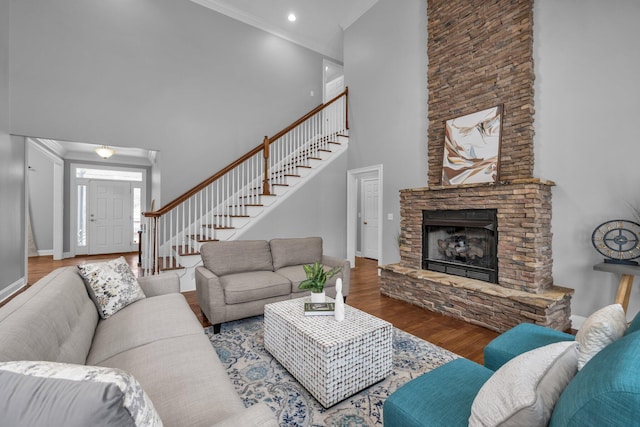 living room featuring a towering ceiling, ornamental molding, a fireplace, and hardwood / wood-style floors