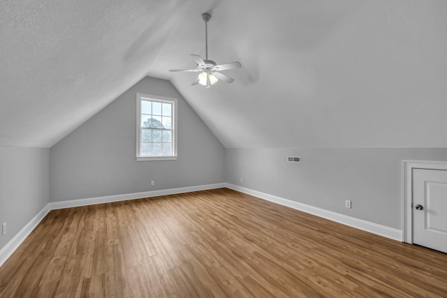 additional living space featuring ceiling fan, lofted ceiling, a textured ceiling, and light hardwood / wood-style floors