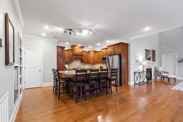 kitchen with an island with sink, a breakfast bar area, backsplash, stainless steel appliances, and light wood-type flooring