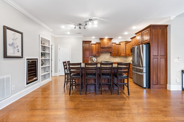 kitchen with wine cooler, a breakfast bar area, wood-type flooring, stainless steel fridge, and a kitchen island with sink