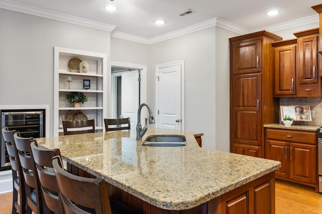 kitchen with sink, a breakfast bar area, light stone counters, light wood-type flooring, and an island with sink