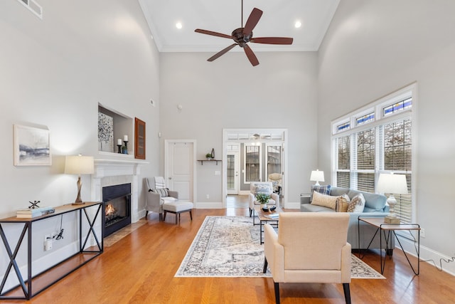 living room with crown molding, wood-type flooring, ceiling fan, a fireplace, and a high ceiling