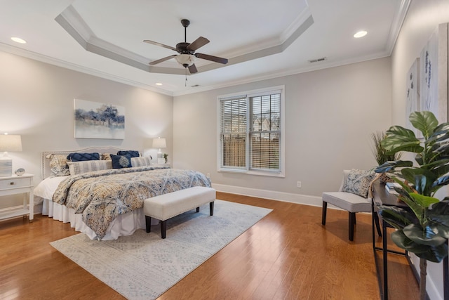 bedroom featuring hardwood / wood-style flooring, crown molding, ceiling fan, and a tray ceiling