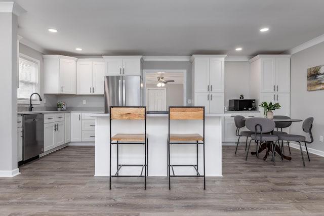 kitchen featuring stainless steel appliances, a breakfast bar, white cabinets, and light countertops