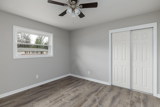 unfurnished bedroom featuring wood finished floors, baseboards, visible vents, ceiling fan, and a closet