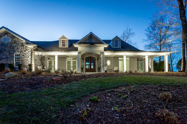 view of front facade with a lawn, covered porch, and french doors