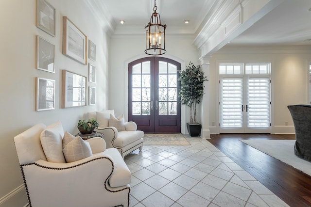 foyer featuring ornamental molding, a towering ceiling, light wood-type flooring, and french doors