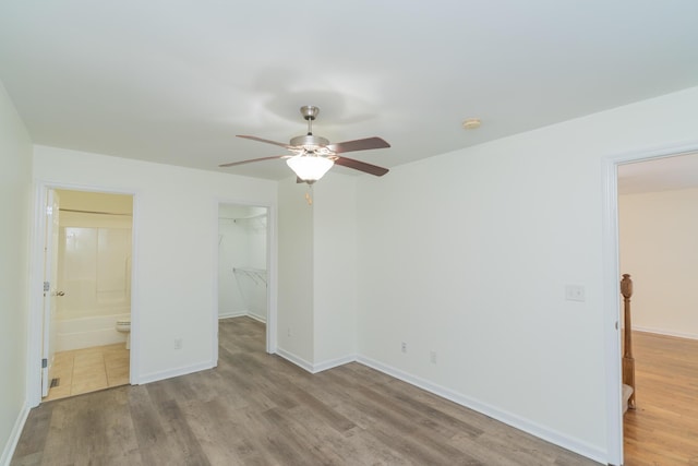 unfurnished bedroom with ensuite bath, a spacious closet, light hardwood / wood-style flooring, a closet, and ceiling fan