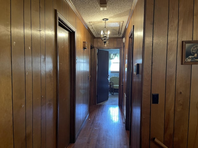 hallway with a chandelier, a textured ceiling, ornamental molding, wooden walls, and dark hardwood / wood-style flooring