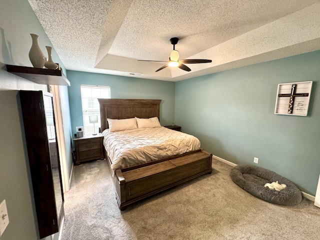 carpeted bedroom with ceiling fan, a raised ceiling, and a textured ceiling