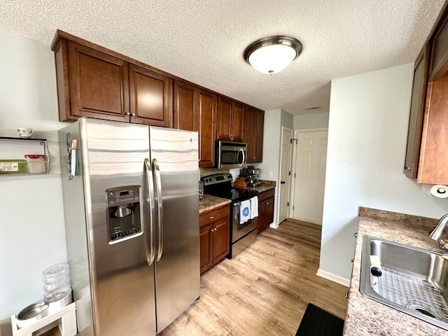 kitchen featuring sink, stainless steel appliances, light hardwood / wood-style floors, and a textured ceiling