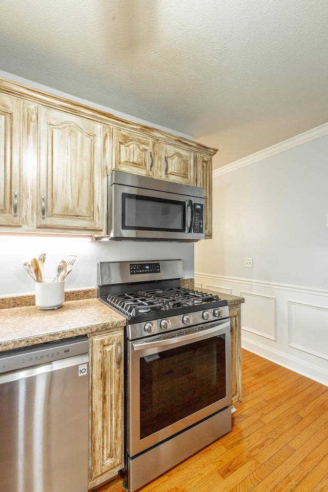 kitchen featuring crown molding, stainless steel appliances, light brown cabinets, and light wood-type flooring