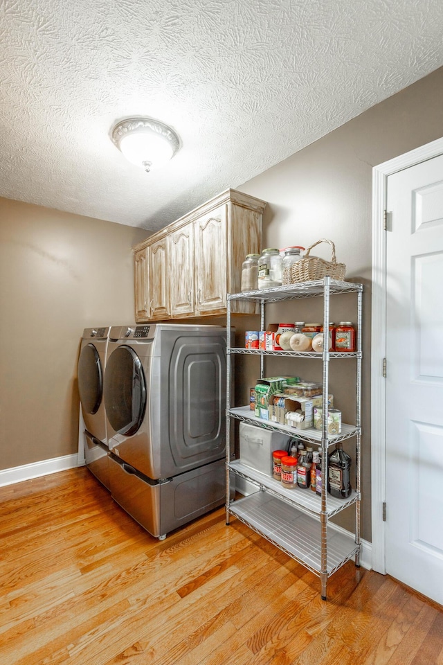 clothes washing area with cabinets, washer and dryer, a textured ceiling, and light hardwood / wood-style flooring