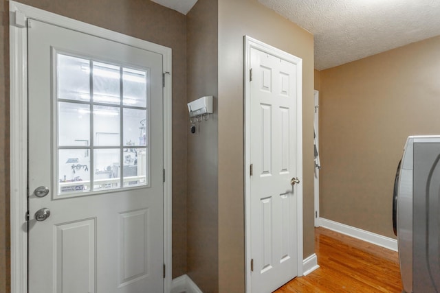 doorway with washer / clothes dryer, a textured ceiling, and light wood-type flooring