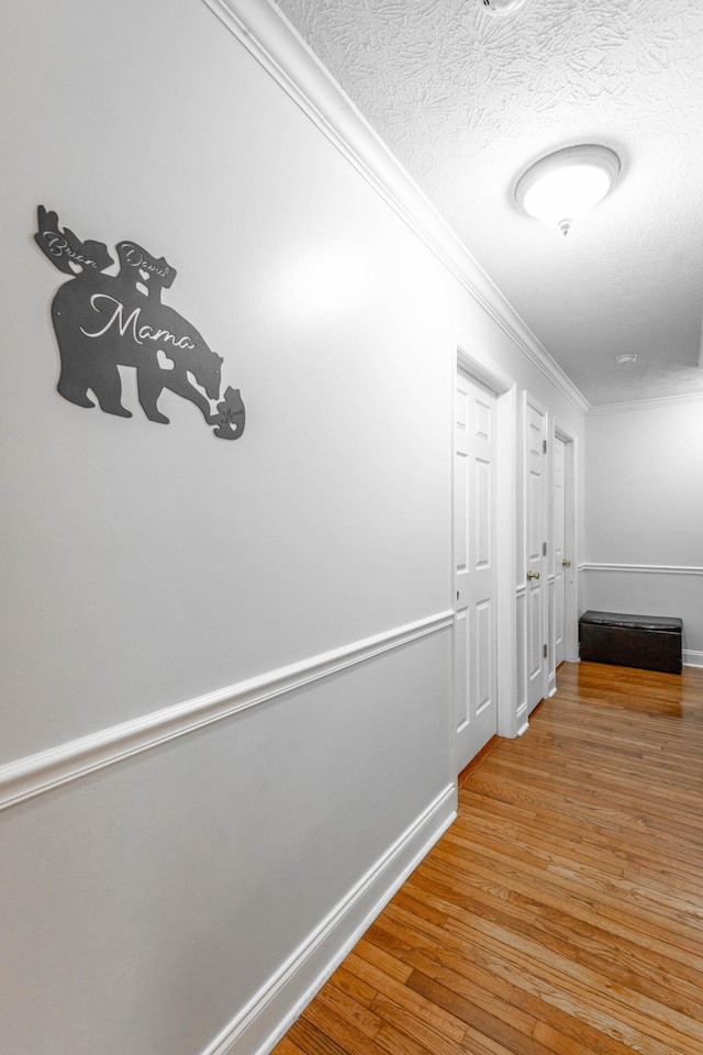 corridor with wood-type flooring, ornamental molding, and a textured ceiling