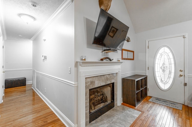 entrance foyer with ornamental molding, a fireplace, vaulted ceiling, and light wood-type flooring