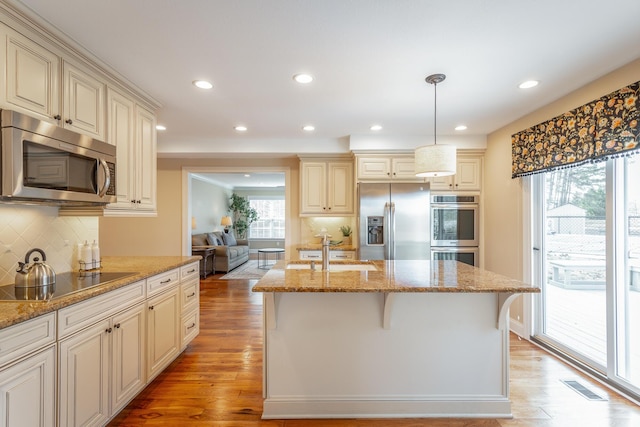 kitchen featuring appliances with stainless steel finishes, decorative light fixtures, a kitchen bar, and light wood-type flooring