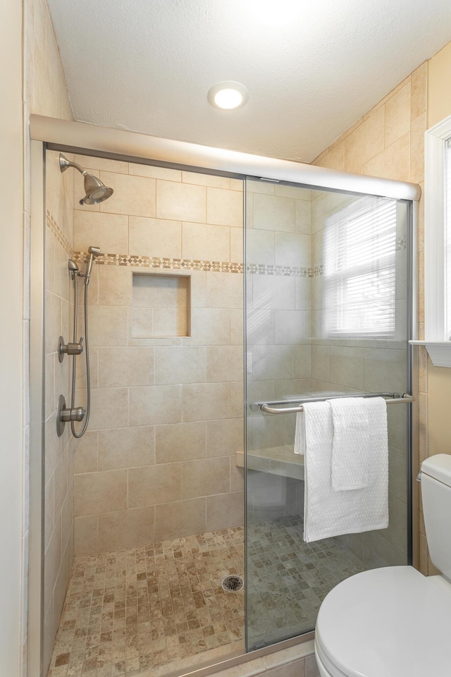 bathroom featuring a shower with door and toilet