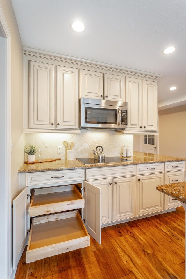 kitchen with light stone countertops, black electric stovetop, backsplash, and light wood-type flooring