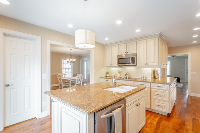 kitchen with pendant lighting, sink, appliances with stainless steel finishes, a kitchen island with sink, and light stone countertops